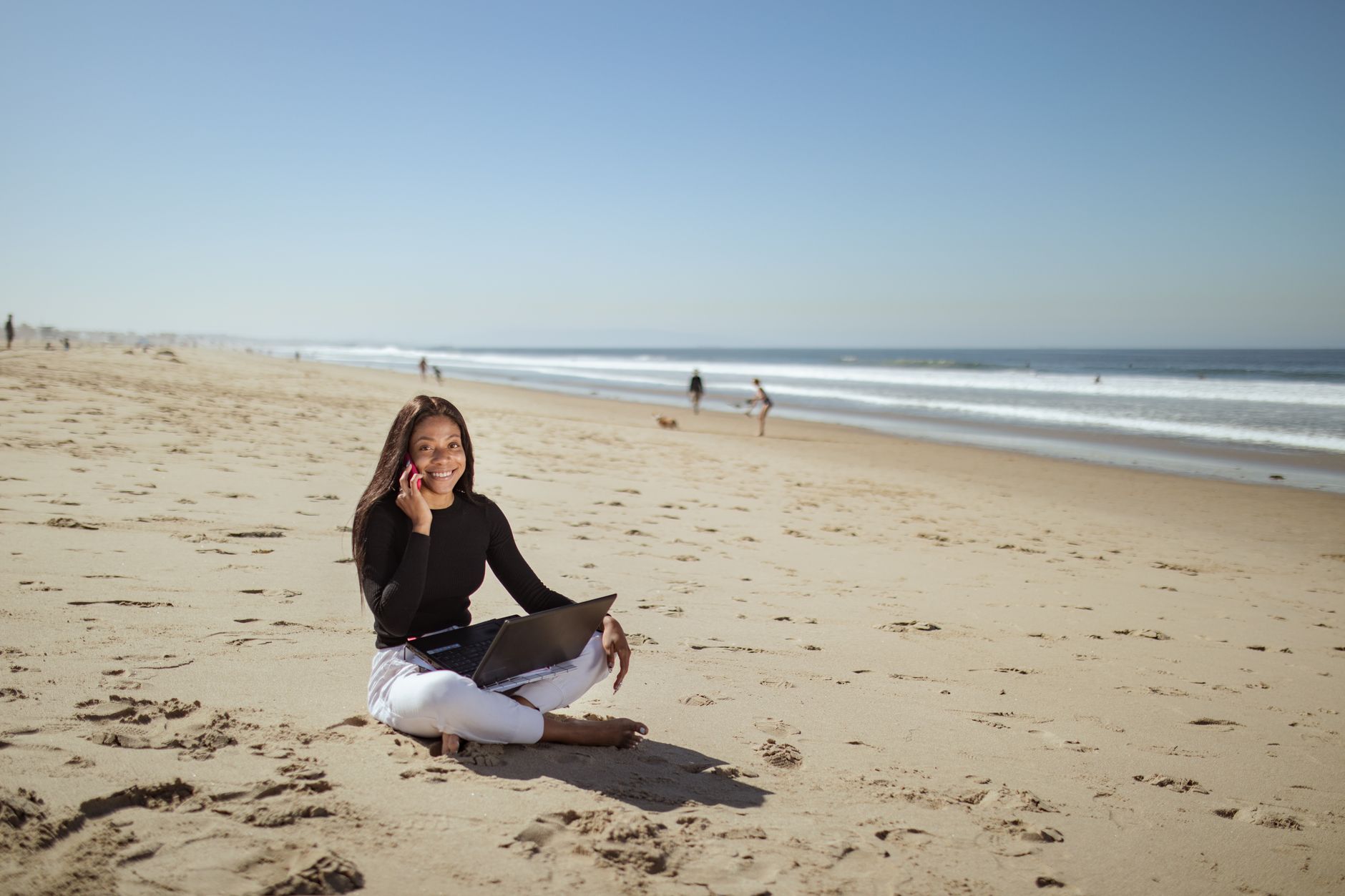 Businesswoman enjoying remote work on a sunny beach using her laptop and smartphone.