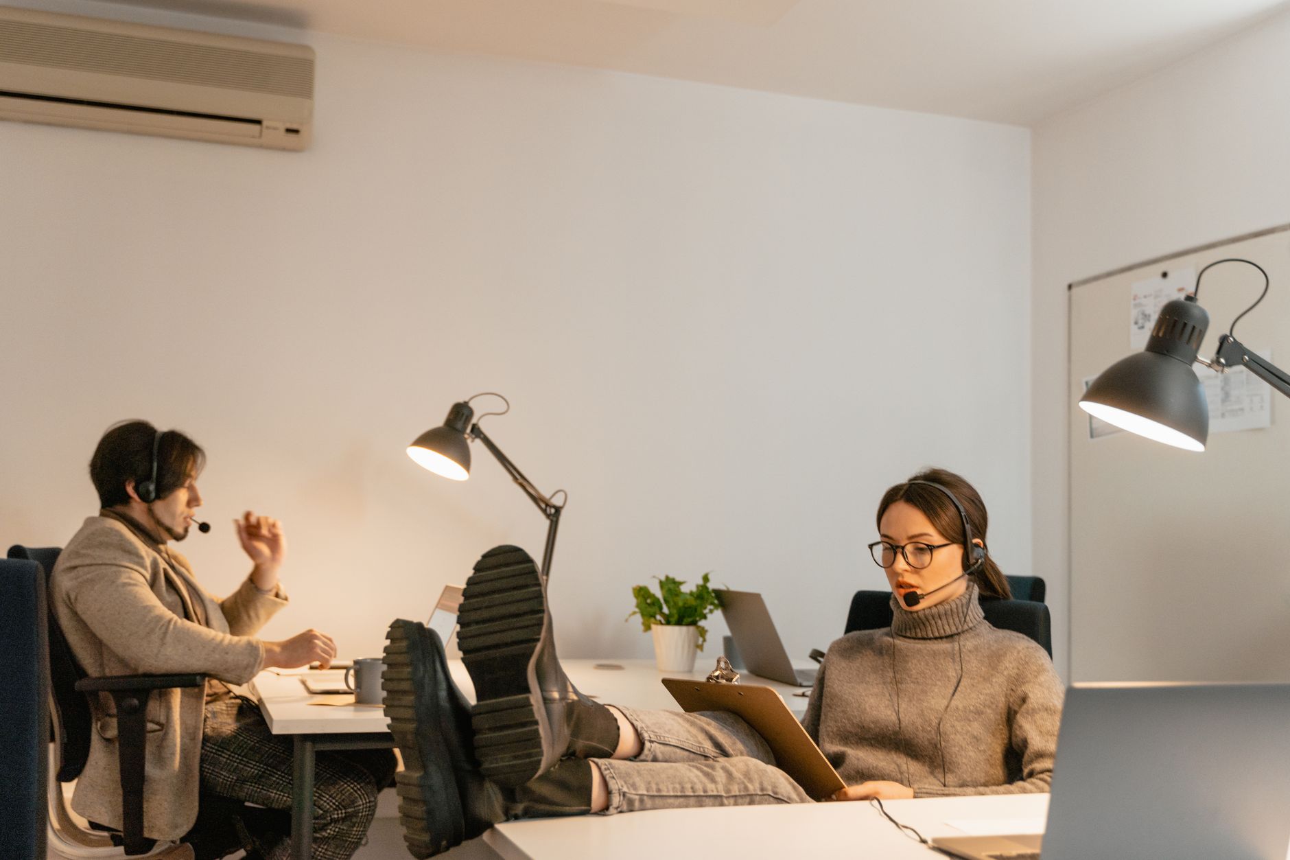 Two call center employees working in a relaxed office environment with headsets and laptops.