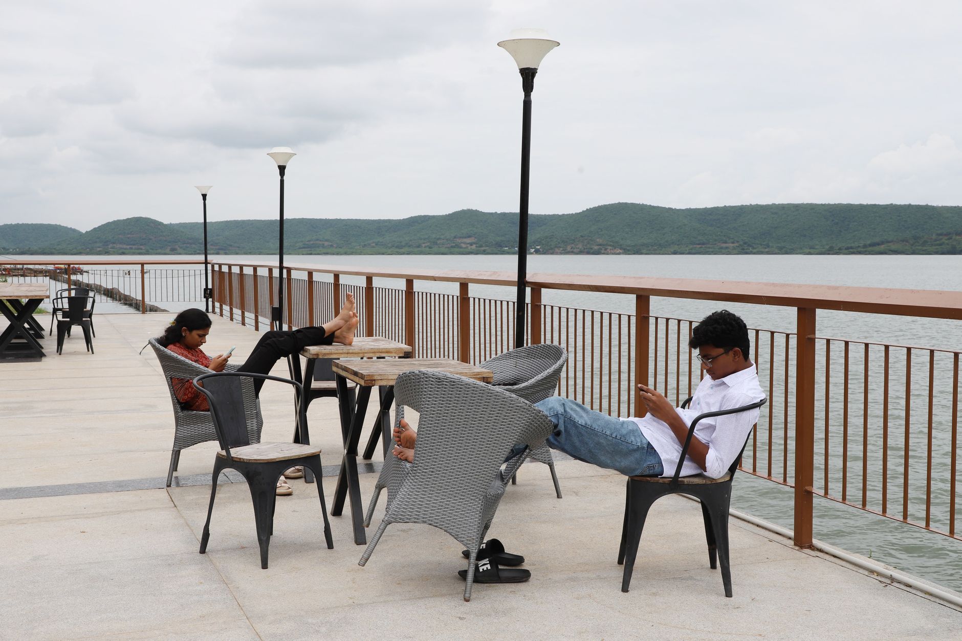 Two adults relax by the lake using their phones, enjoying a peaceful cloudy day.