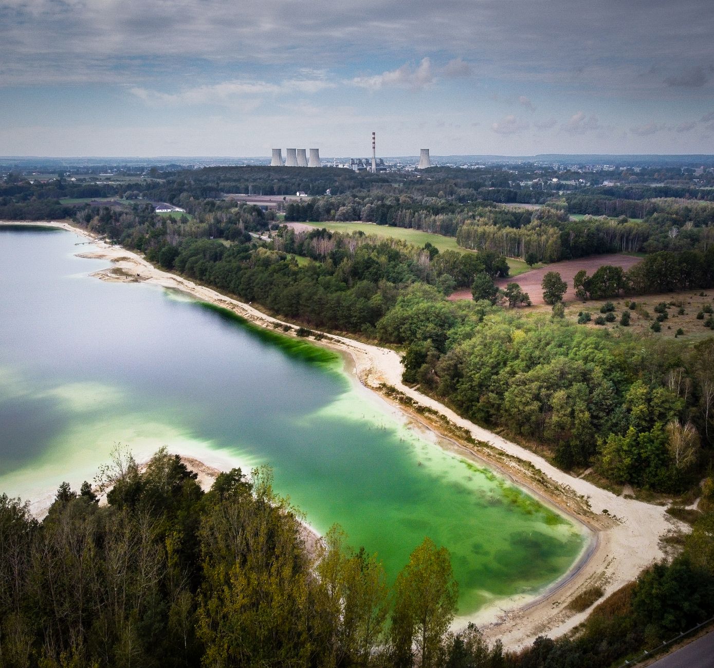 Drone shot of a vibrant green lake near Turek, Poland with a power plant visible in the background.