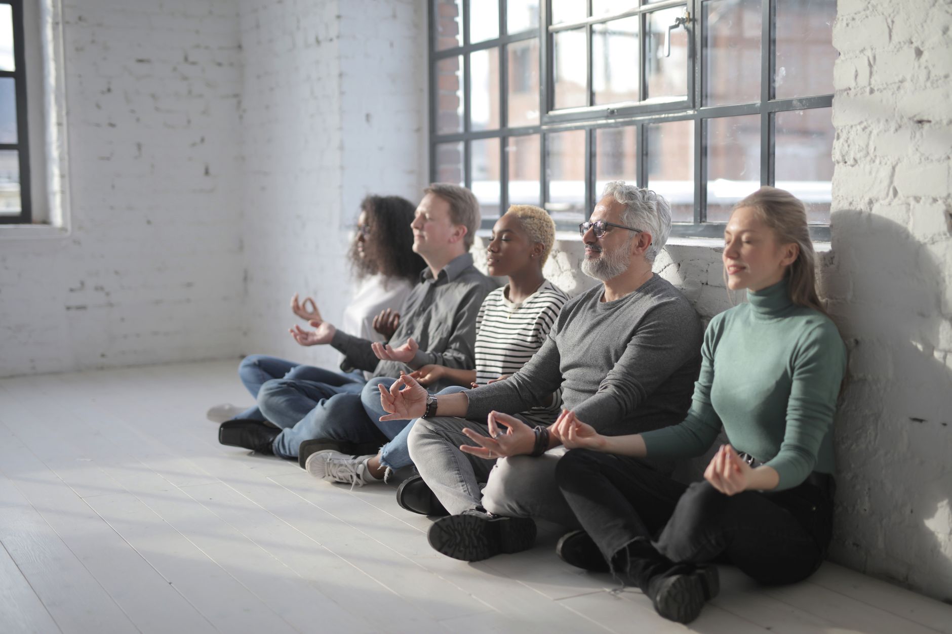 Concentrated multiethnic group of coworkers sitting on floor and having break and meditating all together in modern light office
