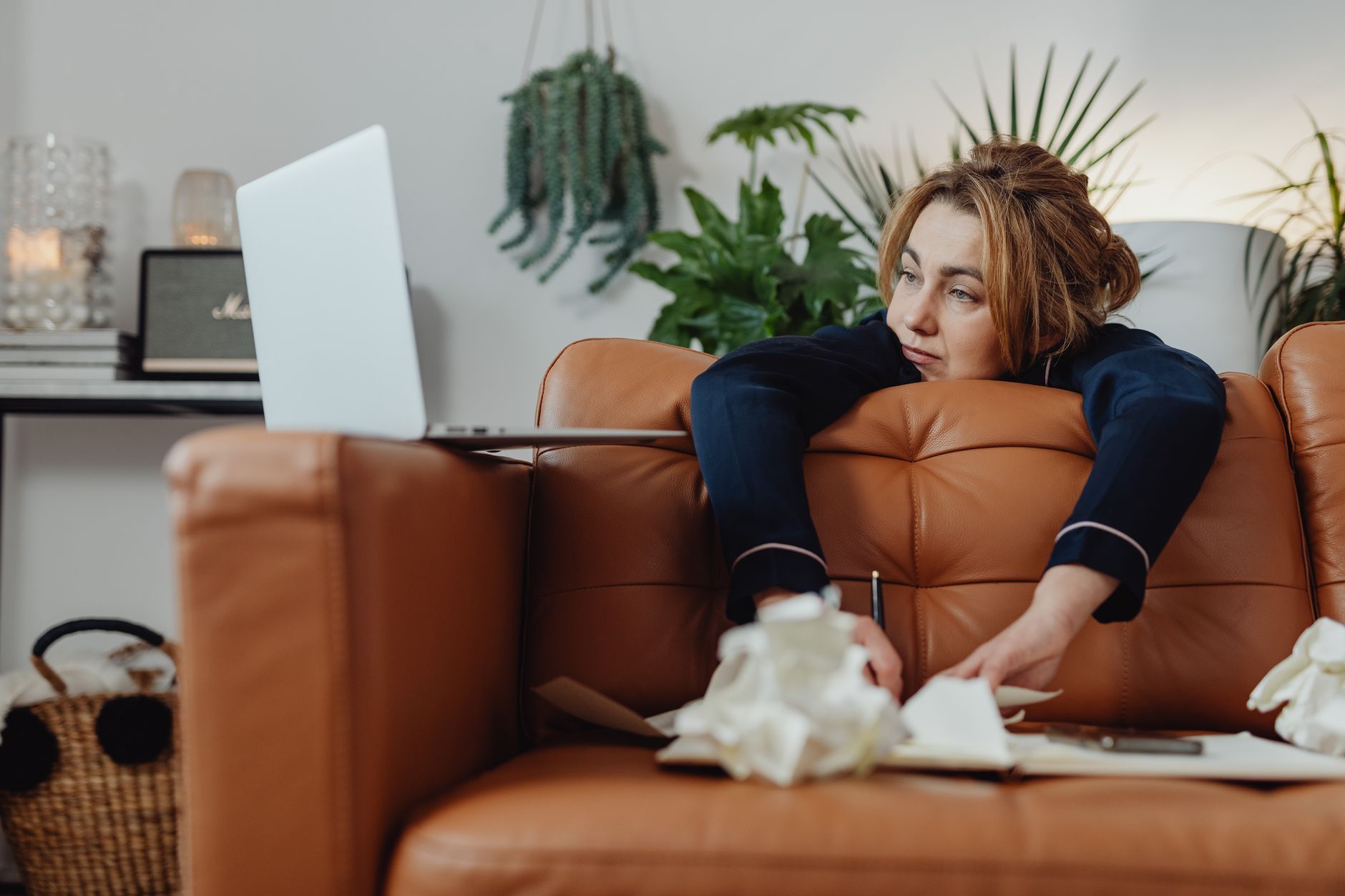 A woman in a home office environment displaying fatigue and stress while working remotely on a laptop.