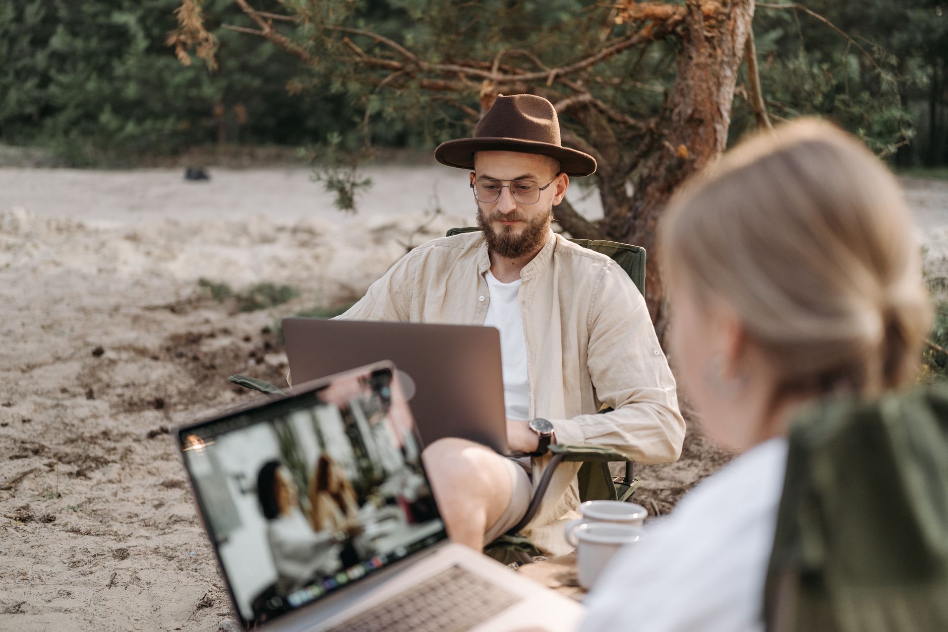 Two digital nomads working on laptops in a peaceful outdoor camping setting.