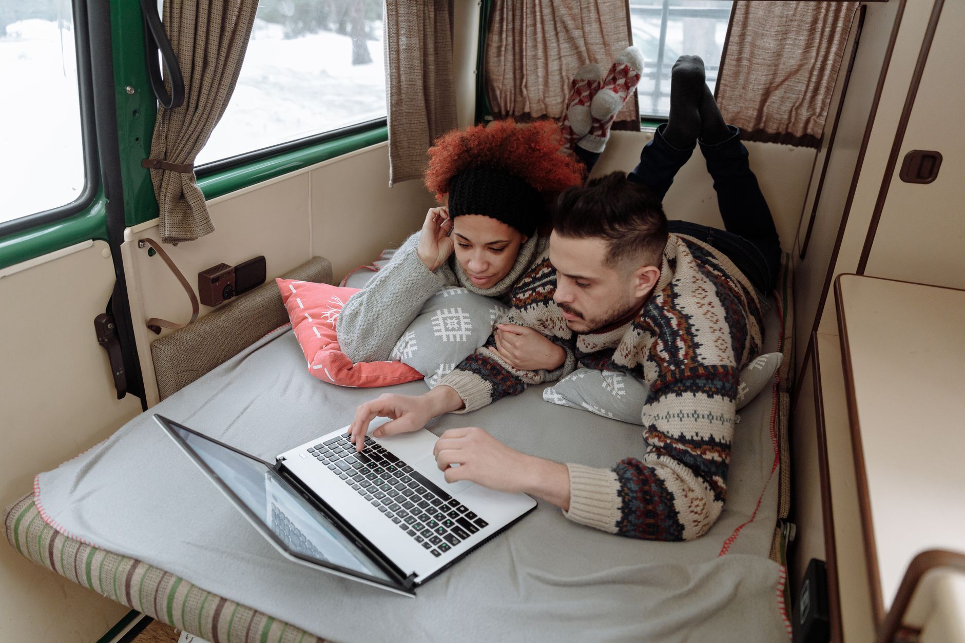 Couple enjoying leisure time in campervan, using laptop in a cozy interior setting.