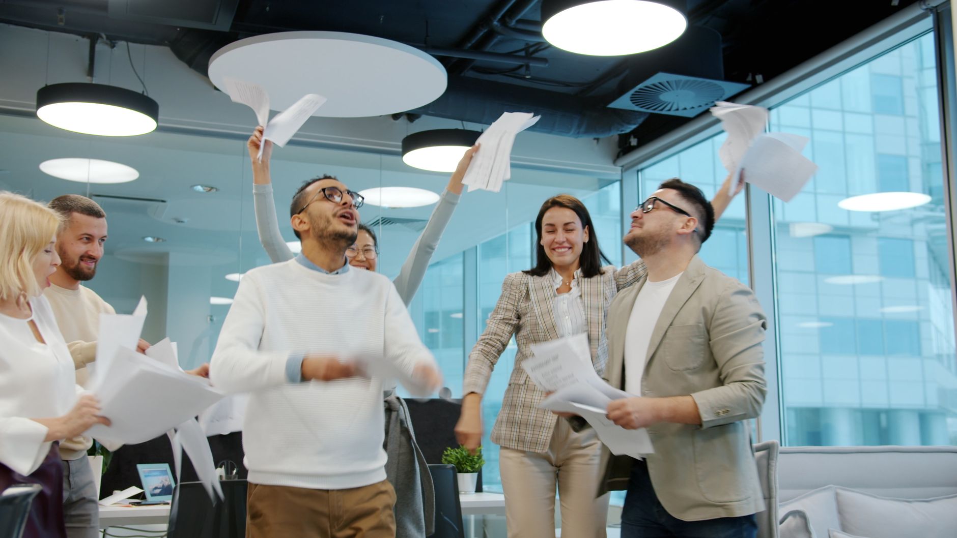 A diverse group of professionals celebrating success in an open-plan office environment.