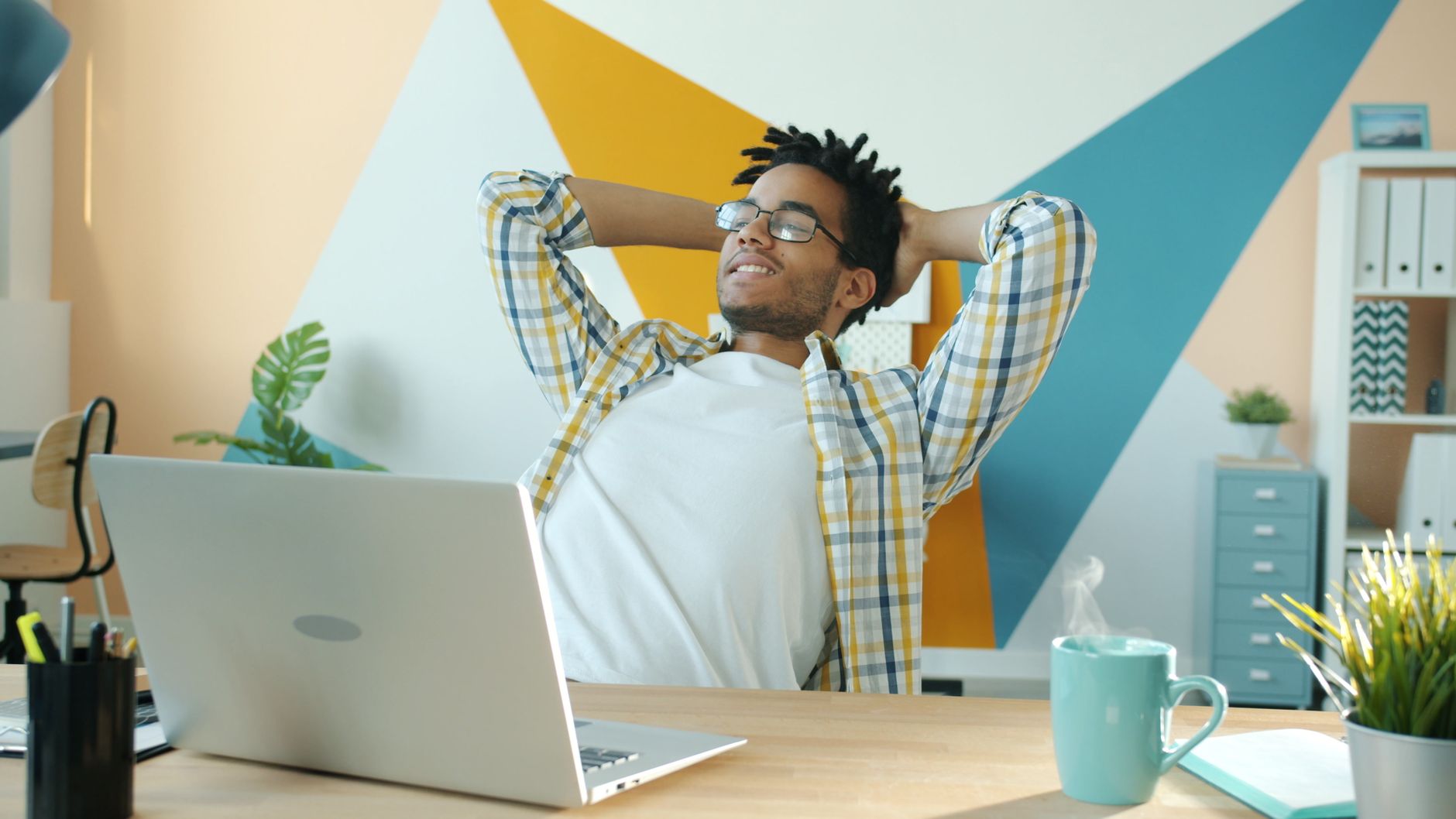 Young man relaxing in colorful modern office with laptop and coffee.