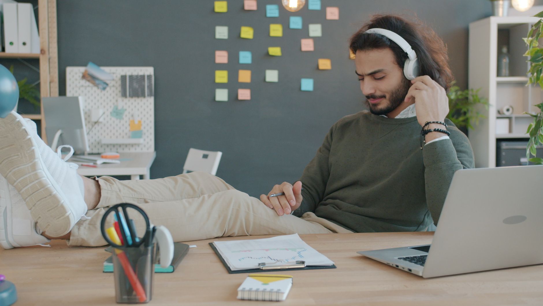 Casual businessman relaxing with headphones and laptop in a creative workspace.