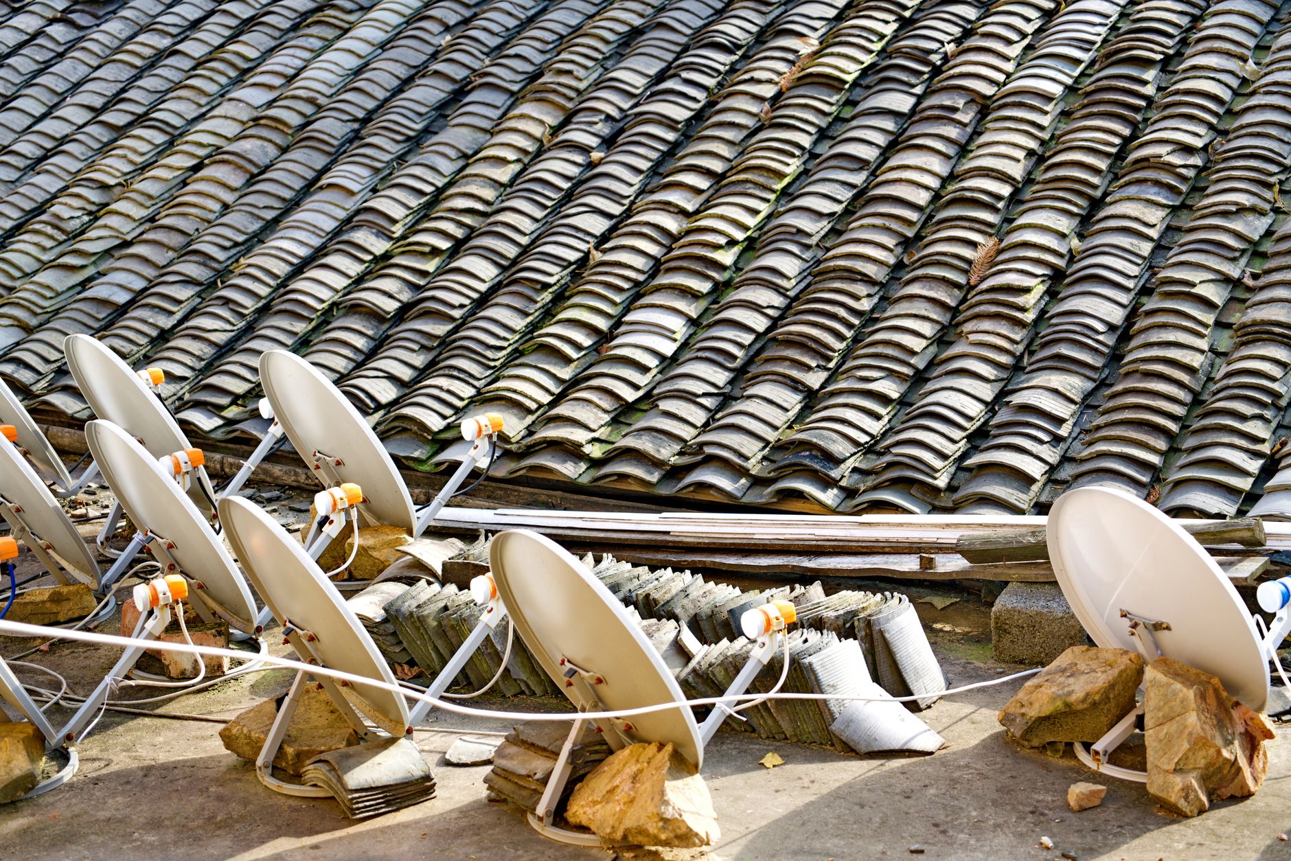 A row of satellite dishes set against an intricately tiled roof, depicting modern technology blending with traditional architecture.